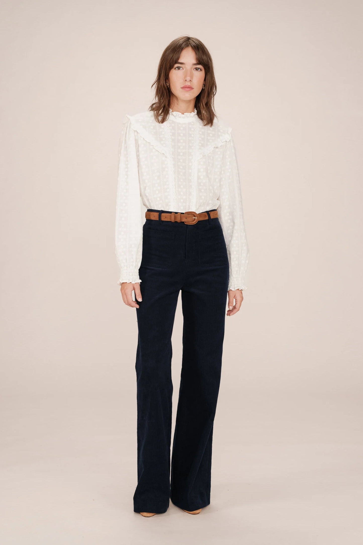 Woman wearing a white blouse and dark blue pants on a beige background