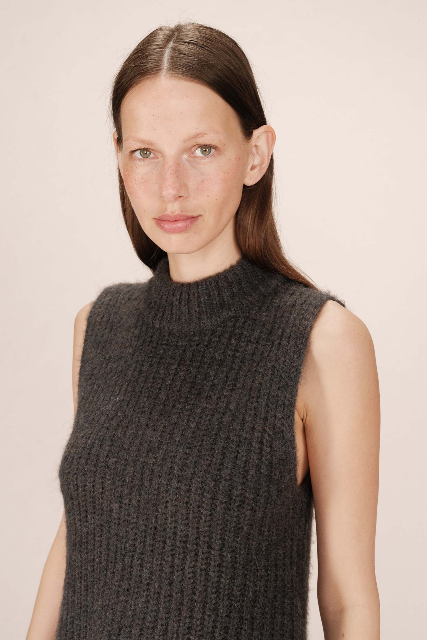 Woman wearing a dark gray knitted sleeveless sweater against a plain background