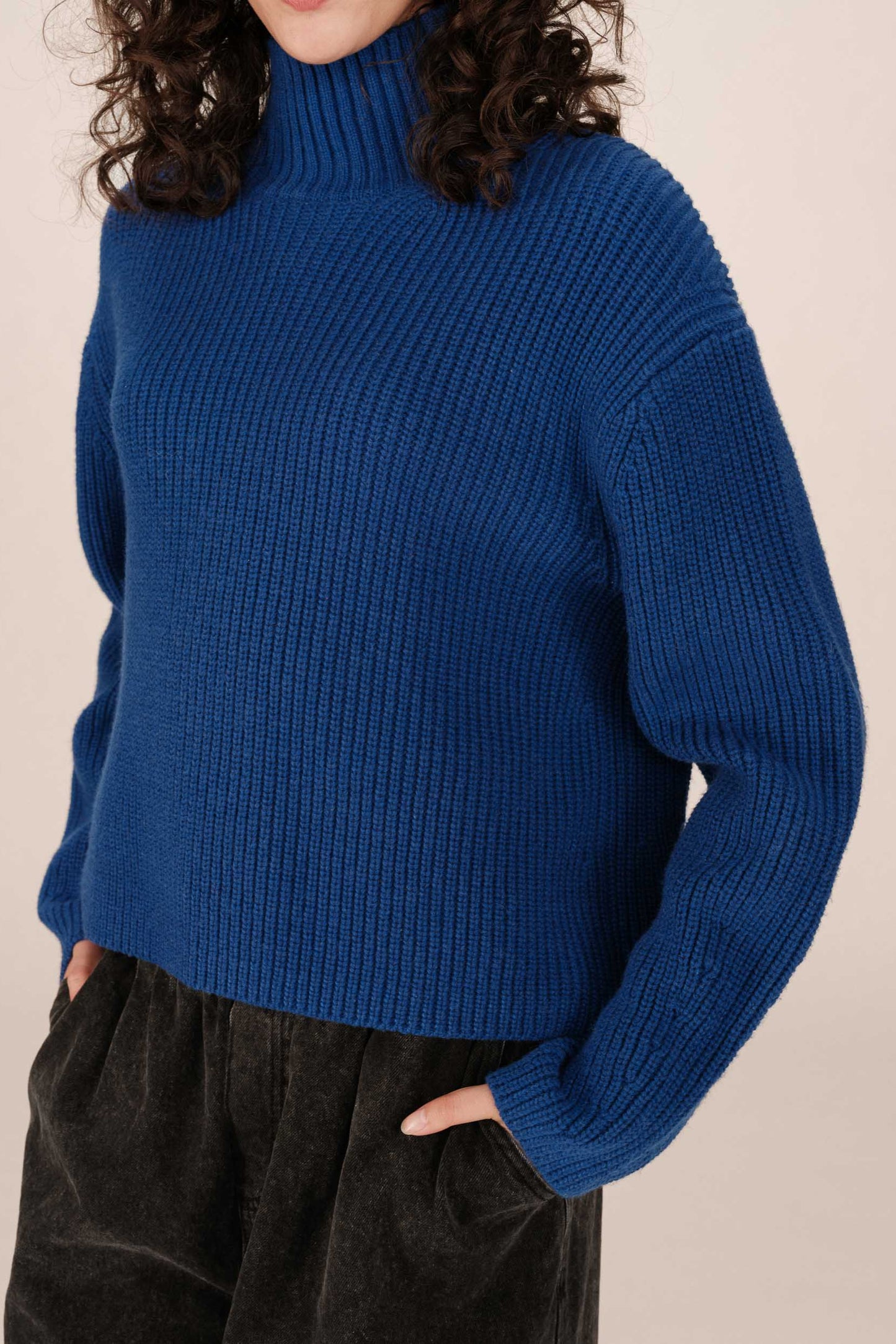 Person wearing a blue ribbed sweater against a beige background