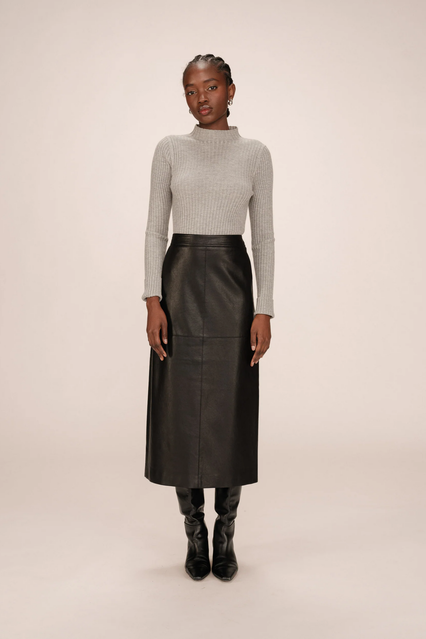 Woman wearing a gray turtleneck and black leather skirt on a beige background