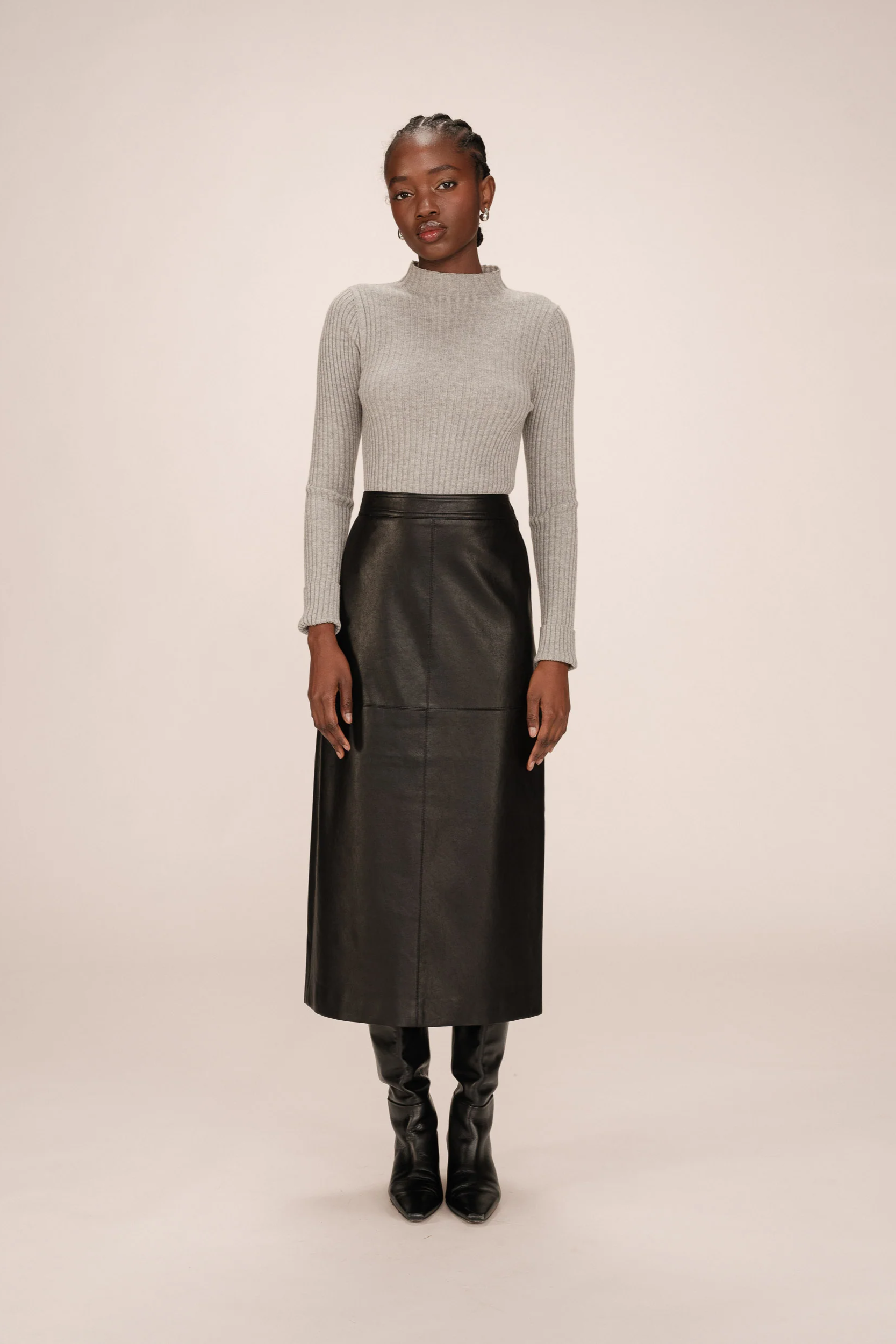 Woman wearing a gray turtleneck and black leather skirt on a beige background