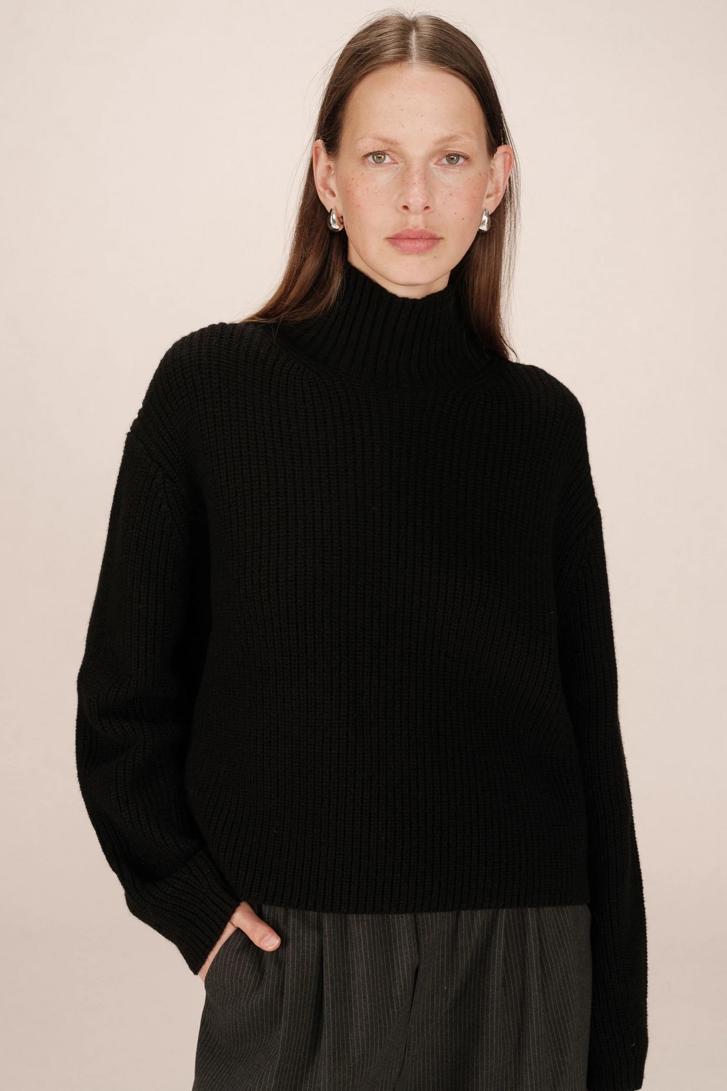 Woman wearing a black turtleneck sweater against a beige background
