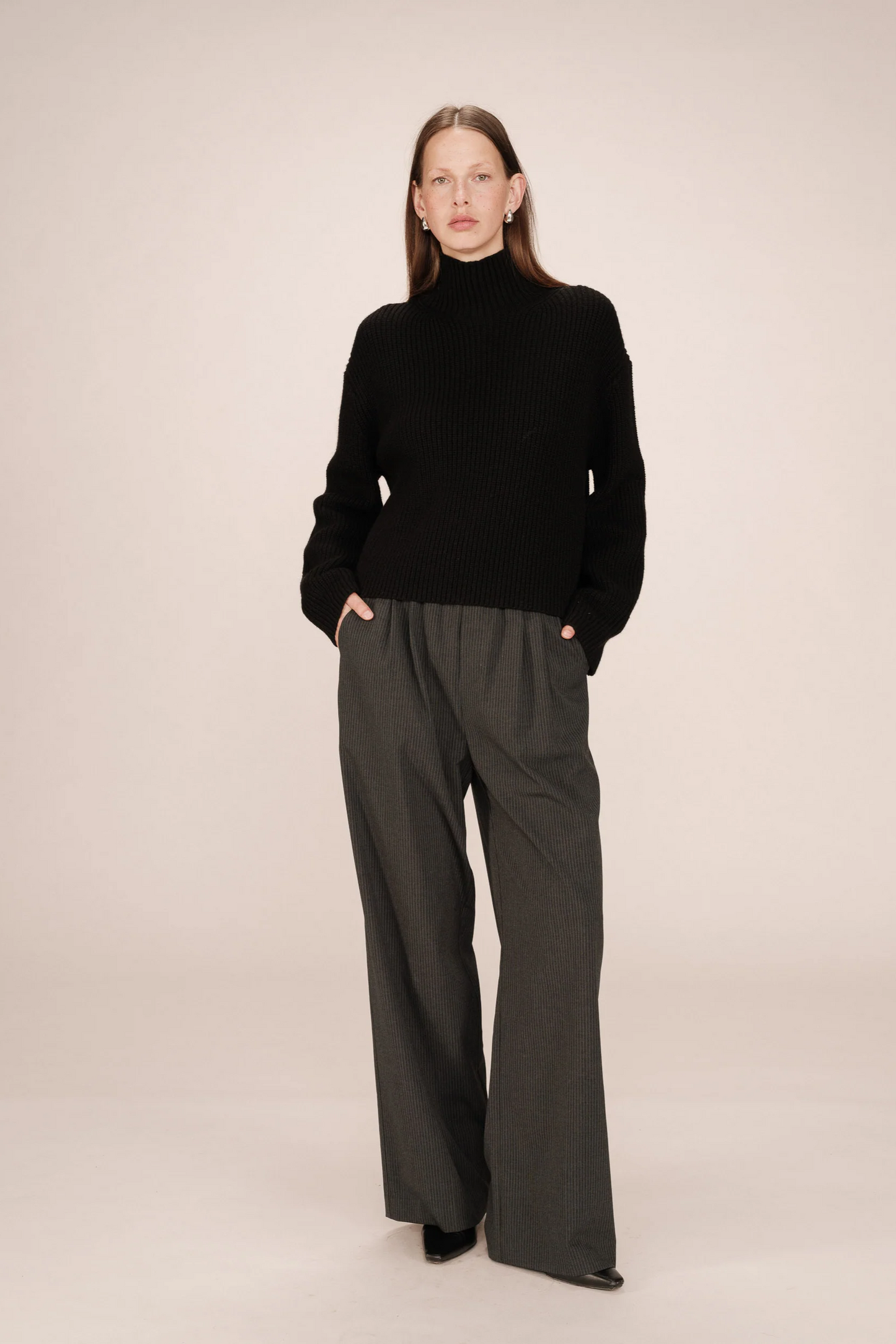 Person wearing a black turtleneck and dark gray wide-leg pants on a beige background