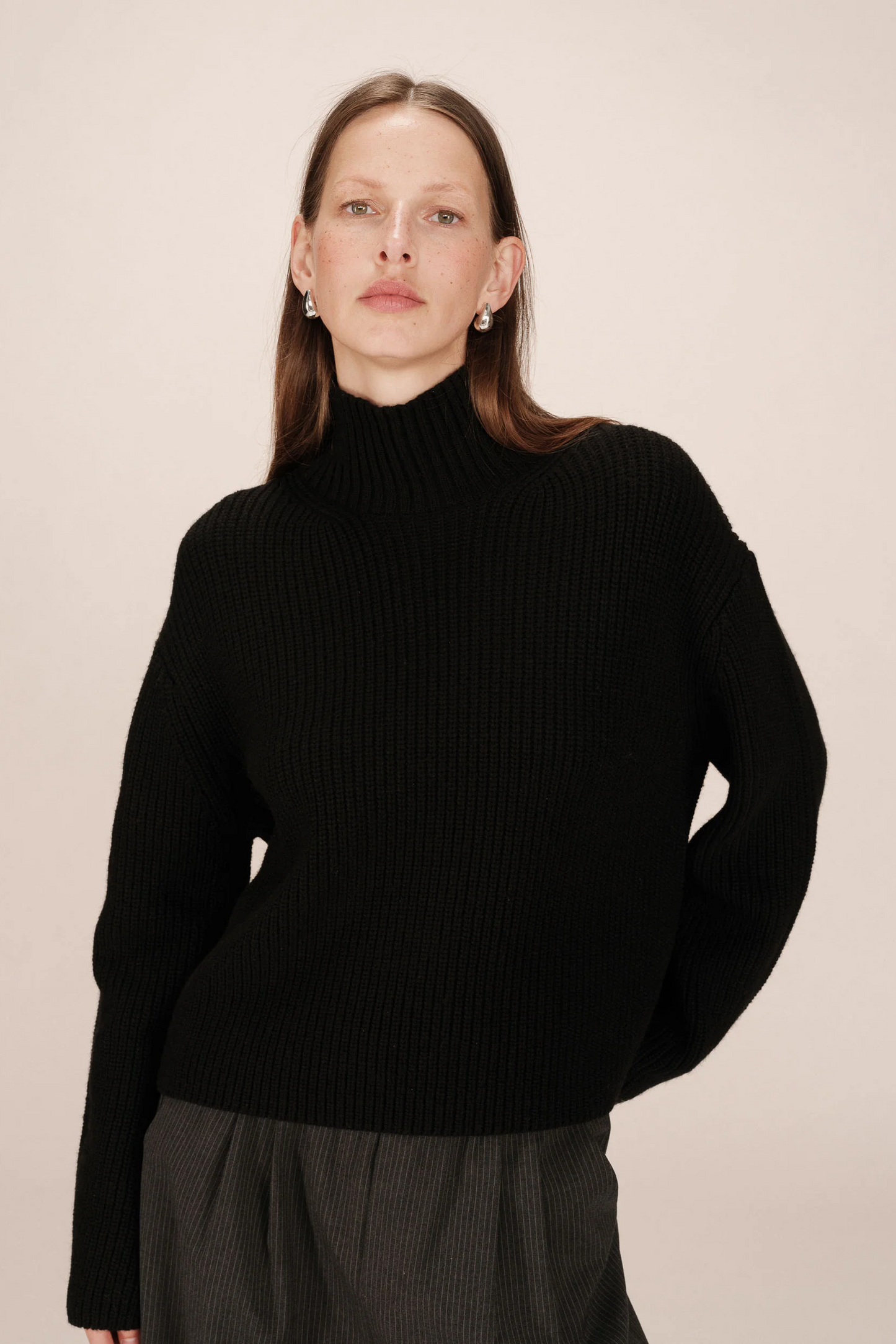 Person wearing a black turtleneck sweater against a beige background