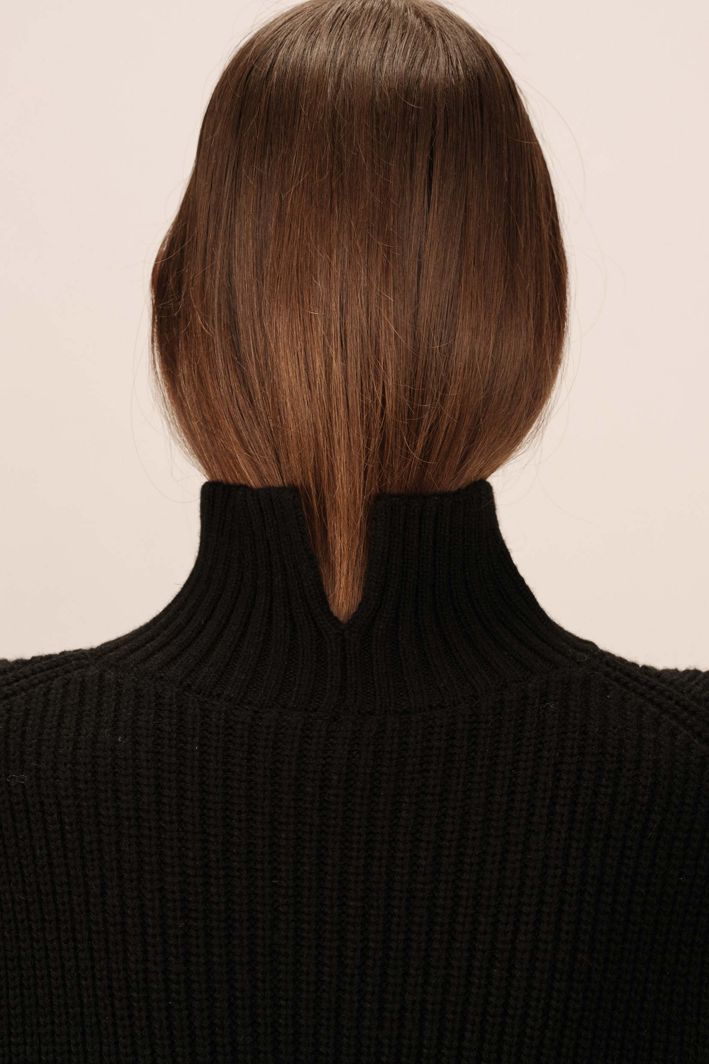 Person wearing a black turtleneck with a stylish haircut on a beige background