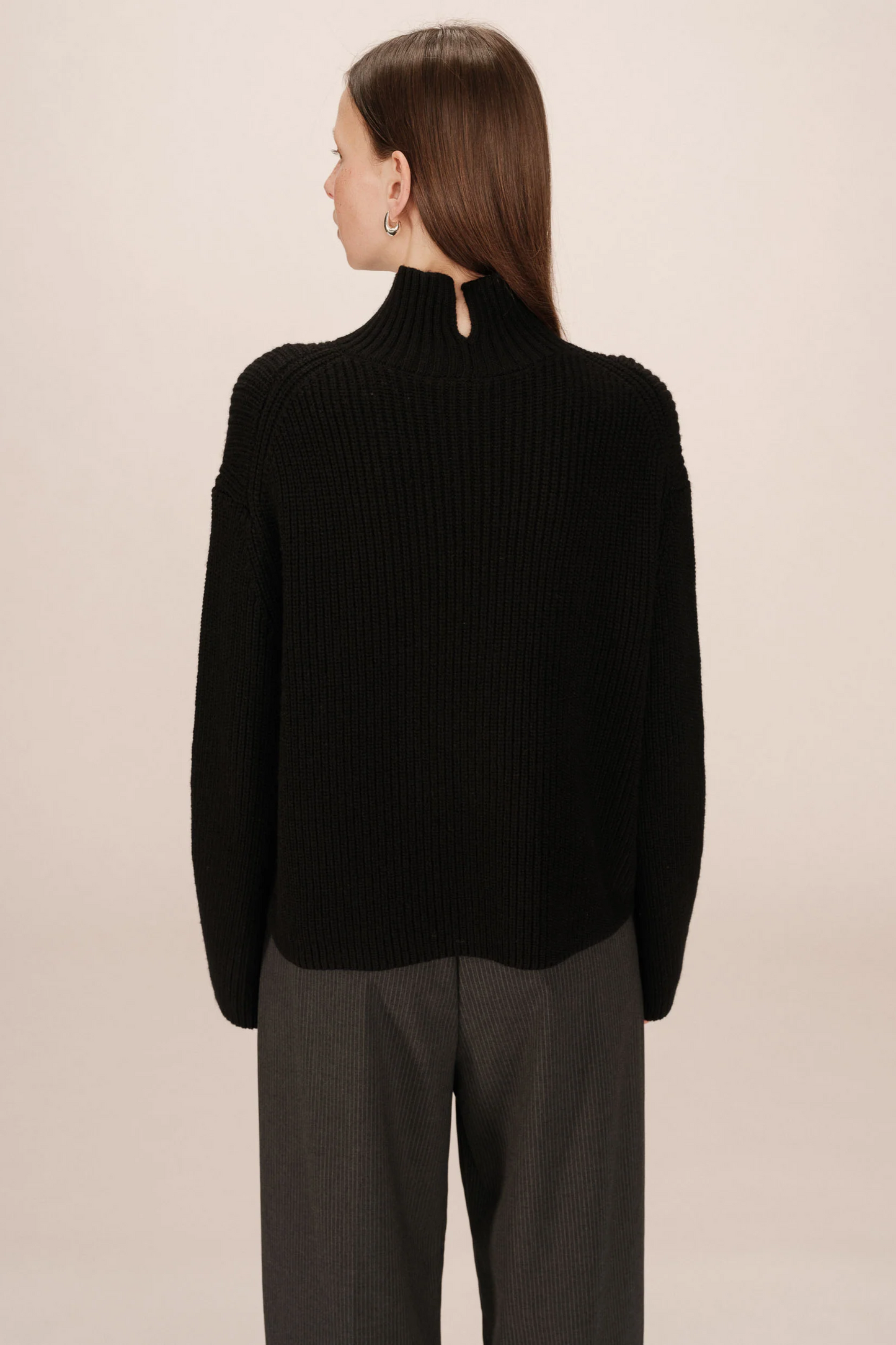 Person wearing a black sweater and gray pants on a beige background