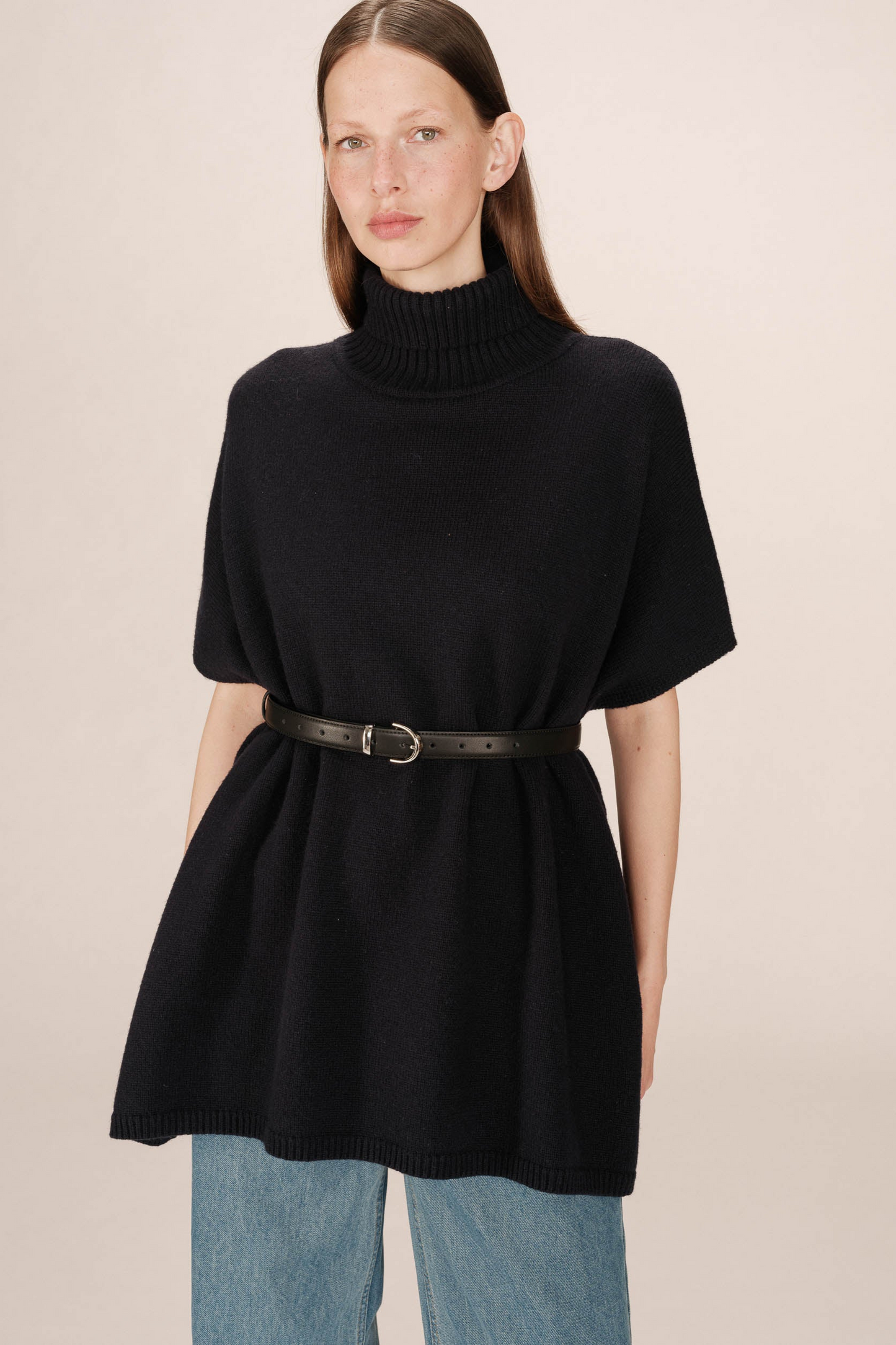 Woman wearing a black turtleneck dress with a belt on a beige background