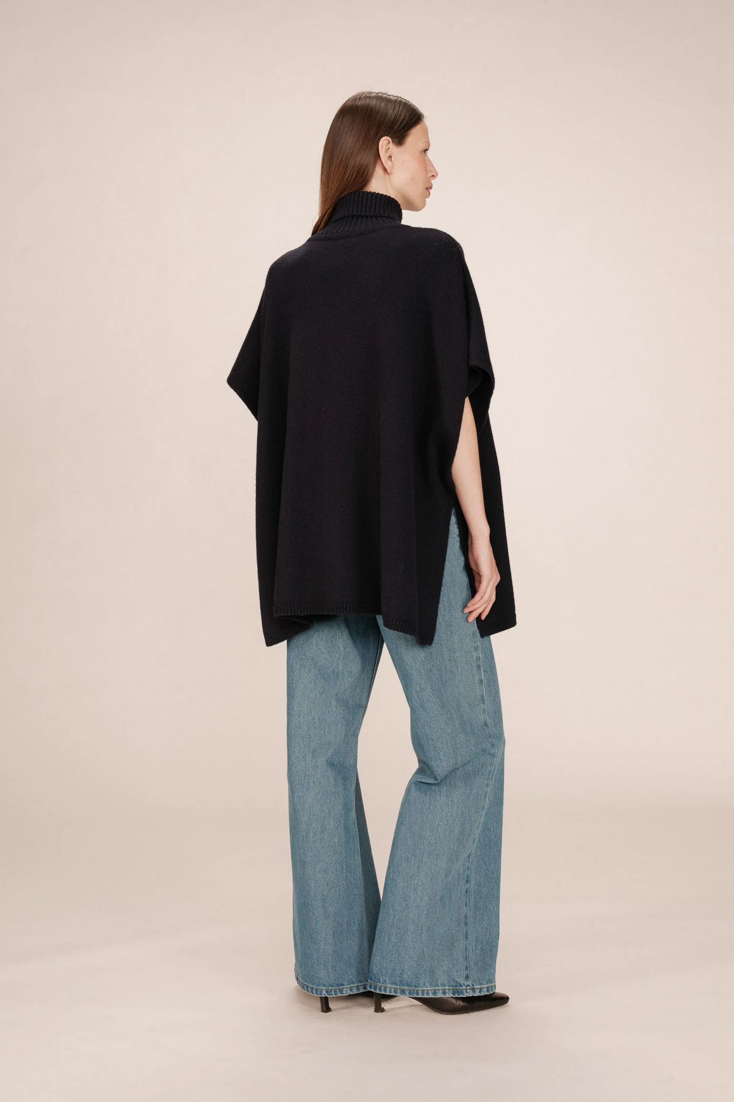 Woman wearing a black poncho and blue jeans on a beige background