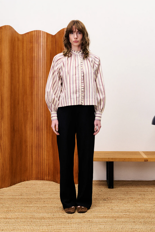 Person wearing a striped shirt and black pants standing in a room with wooden paneling and a bench.
