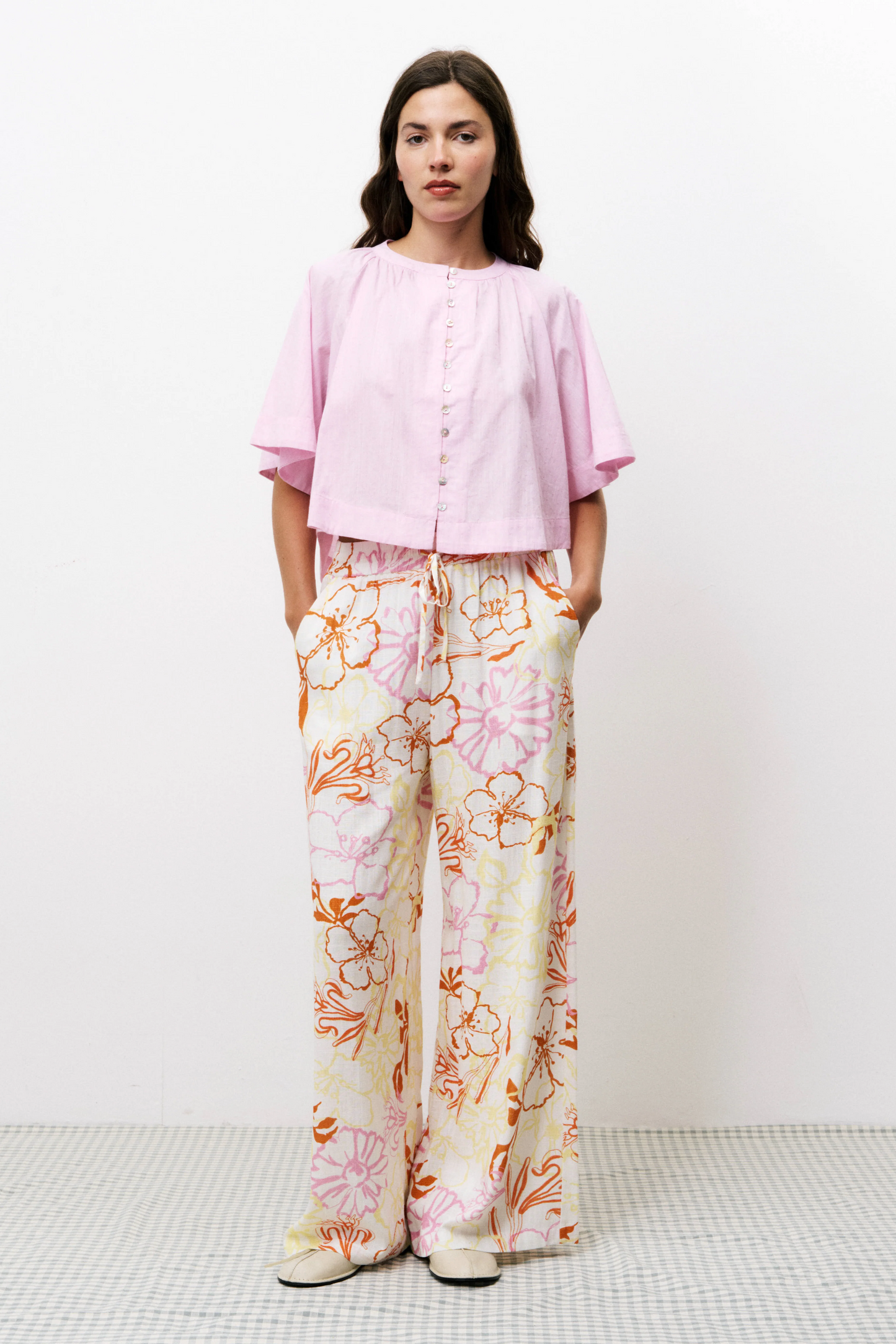 Woman wearing a pink blouse and floral pants on a white background