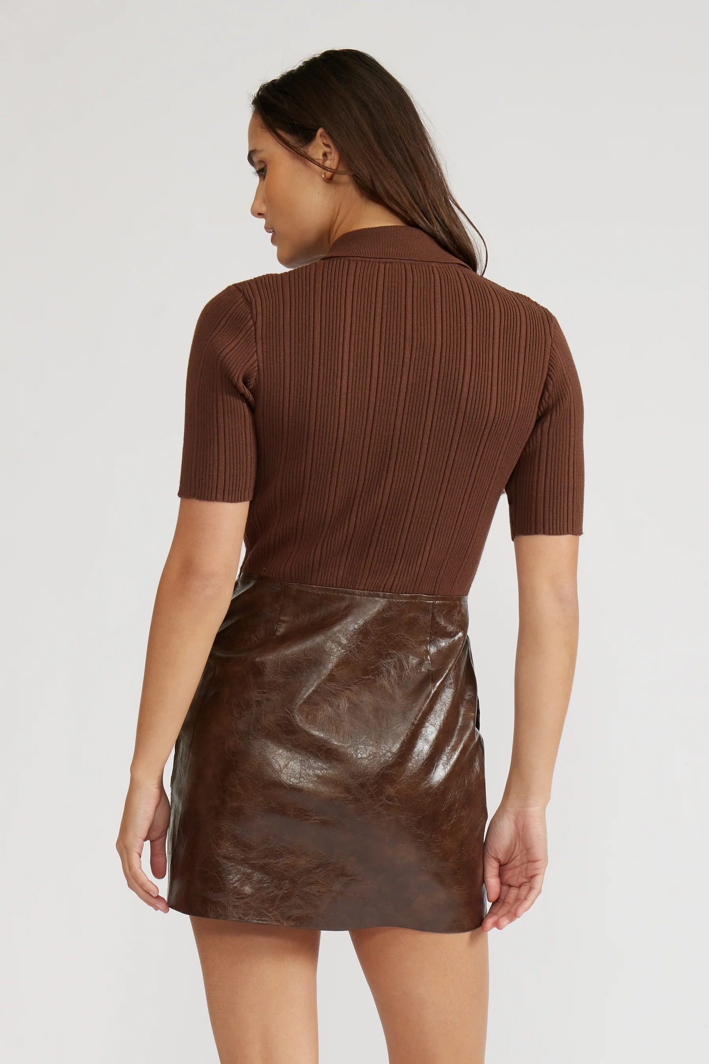 Woman wearing a brown ribbed top and leather skirt on a white background