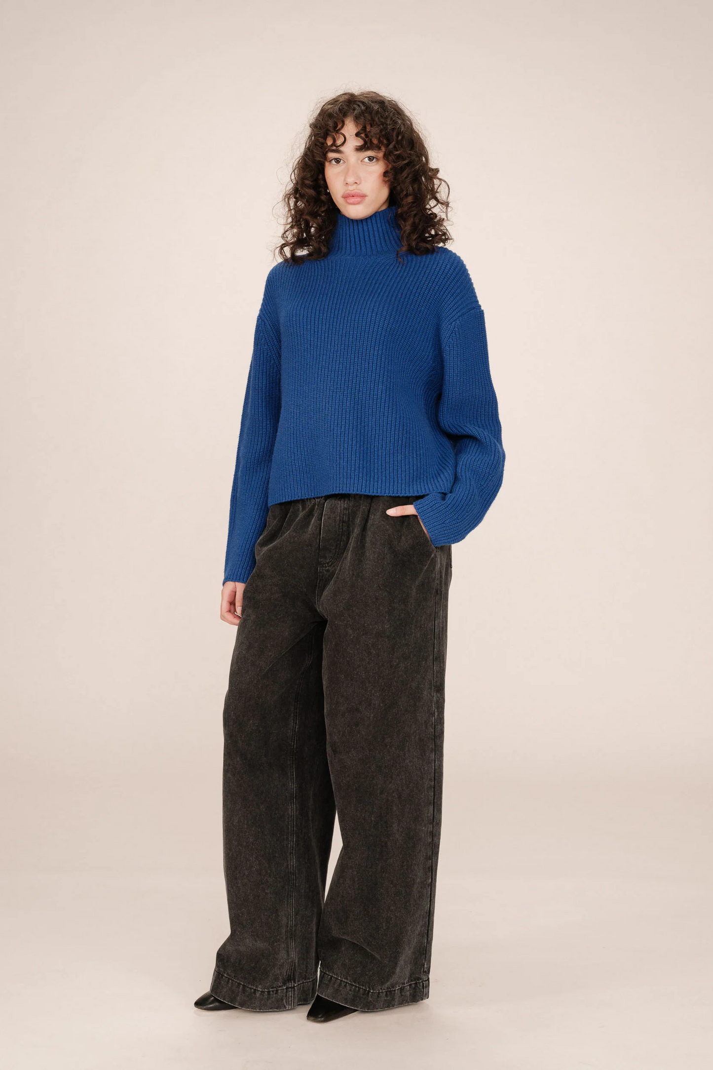 Person wearing a blue sweater and dark pants on a beige background