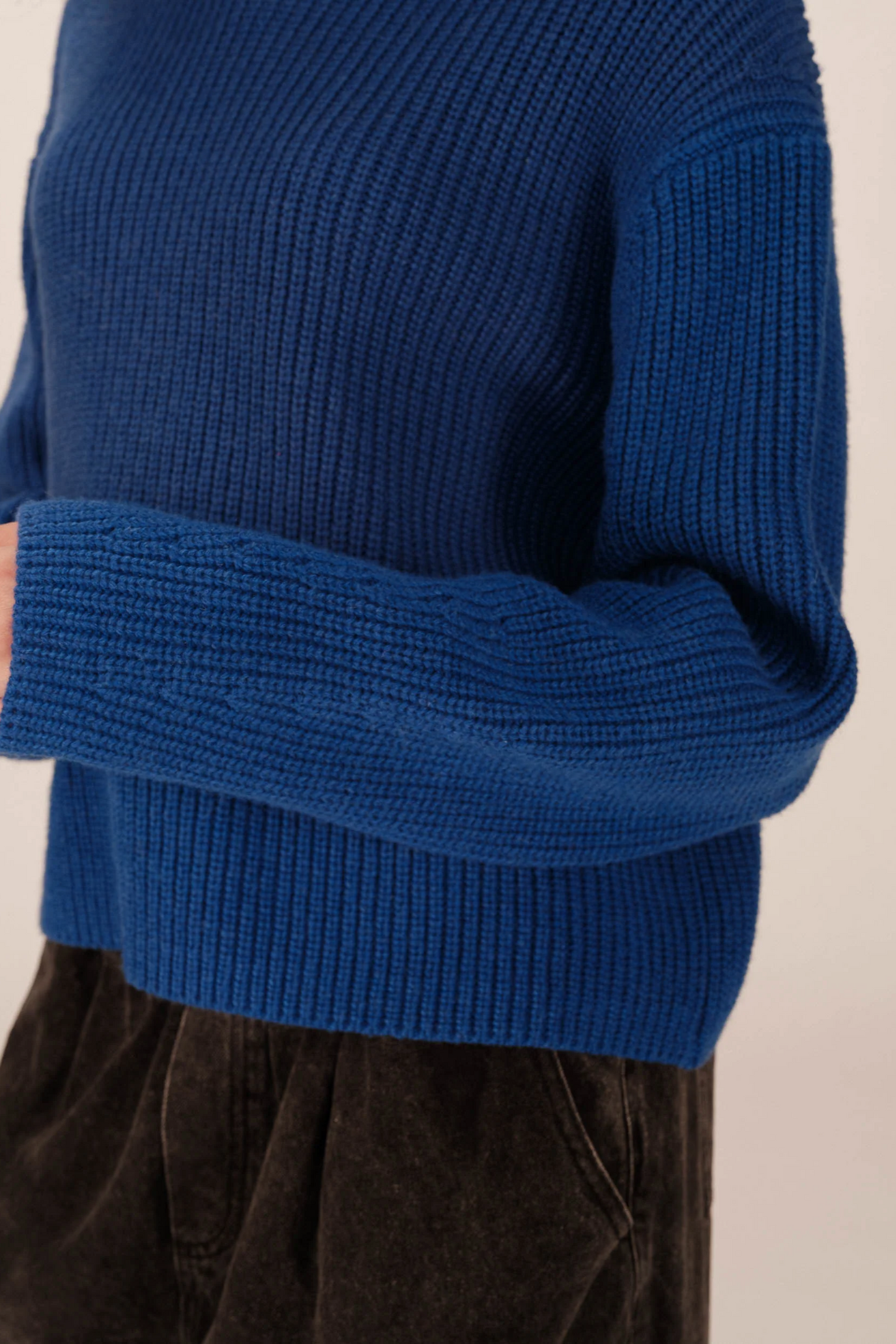 Blue knitted sweater worn by a person on a beige background