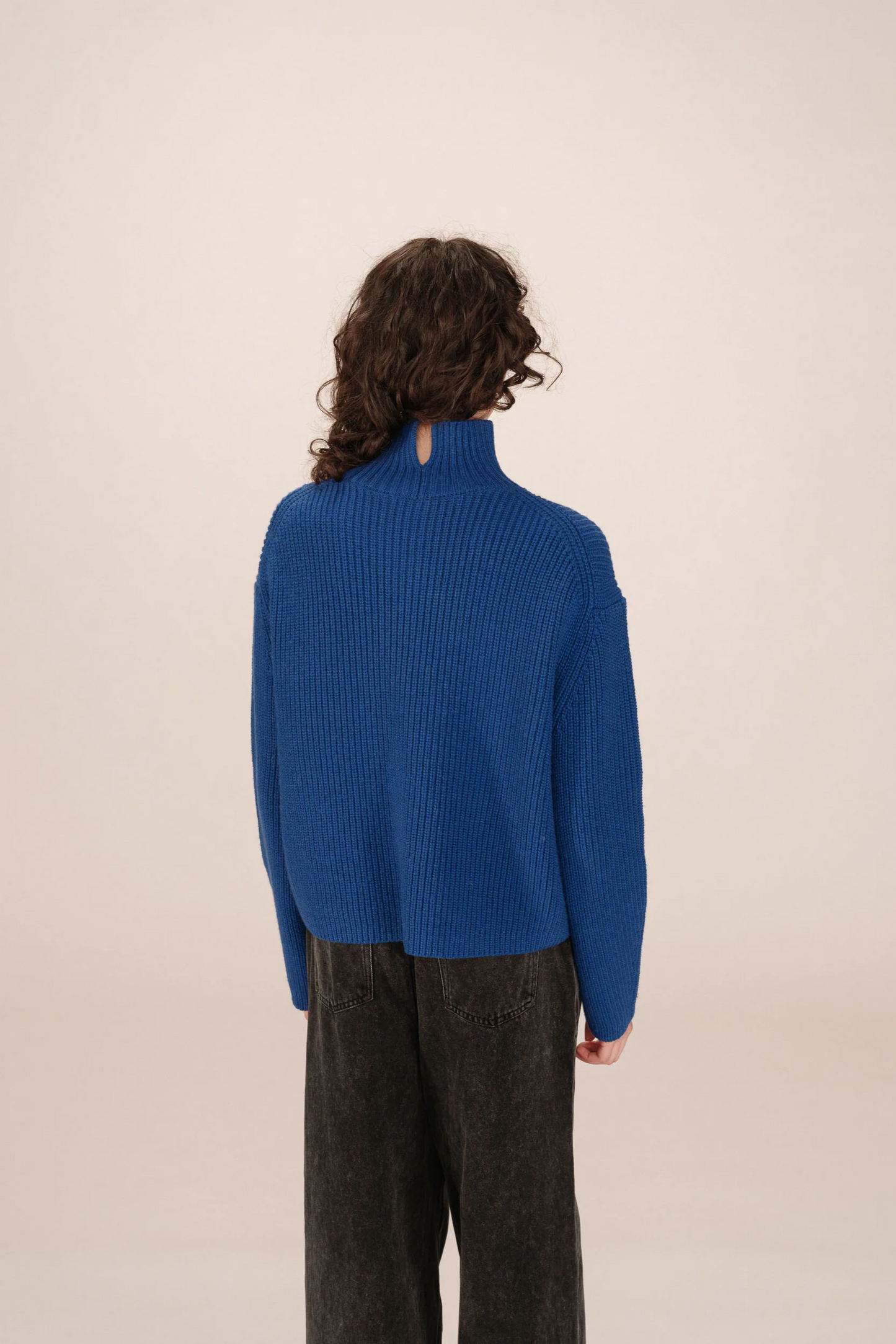 Person wearing a blue sweater and dark pants against a beige background