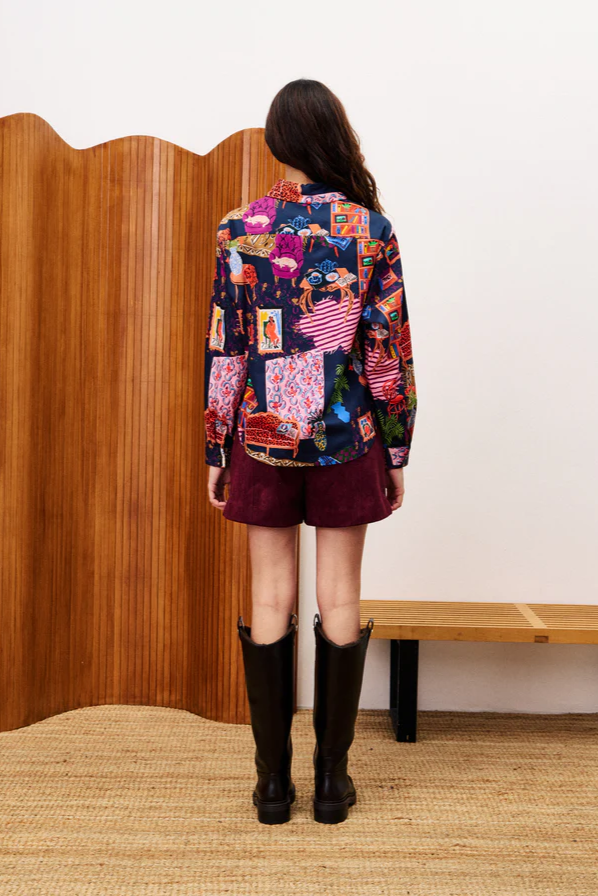 Person wearing a colorful patchwork jacket with a wooden screen and bench in the background