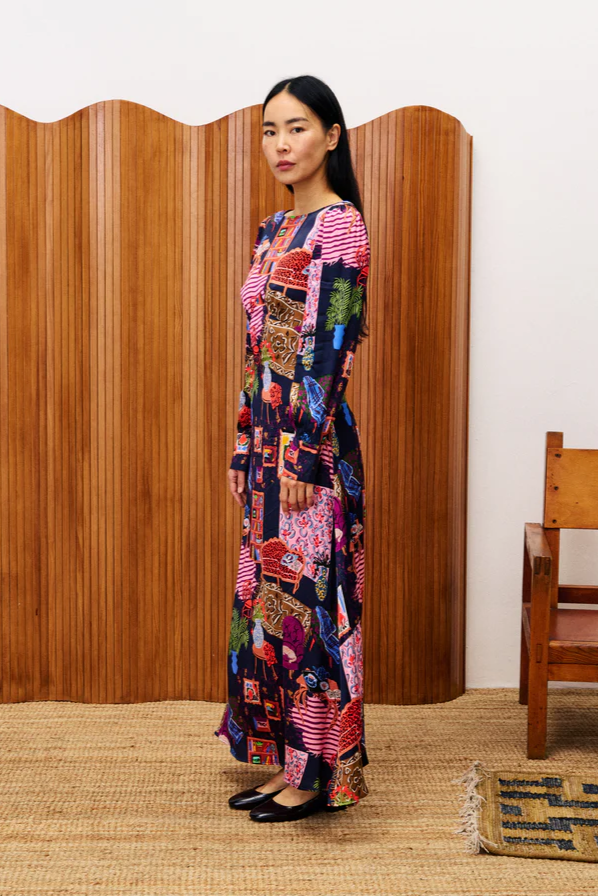 Woman wearing a colorful patchwork dress standing in front of a wooden screen.