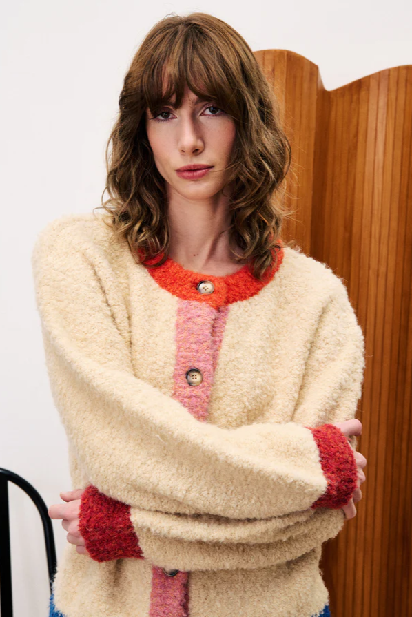 Woman wearing a cream cardigan with red accents in a room with wooden paneling.