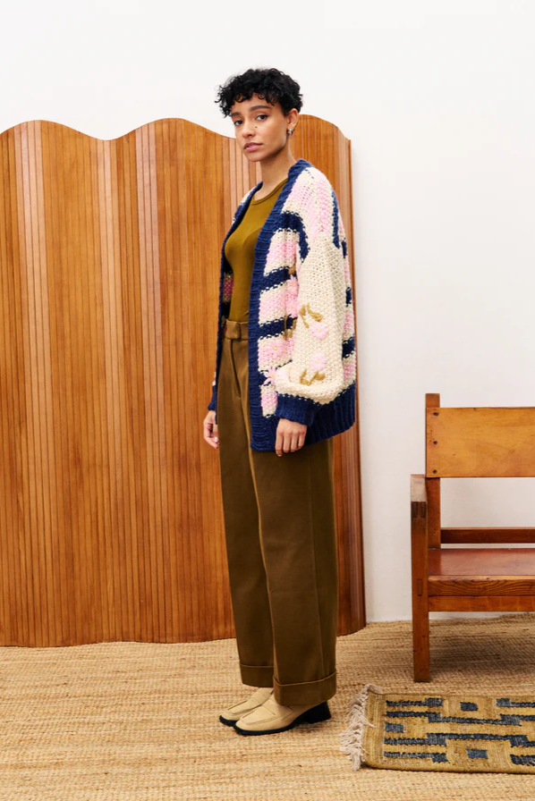 Woman wearing a colorful cardigan in a room with wooden furniture and a rug.