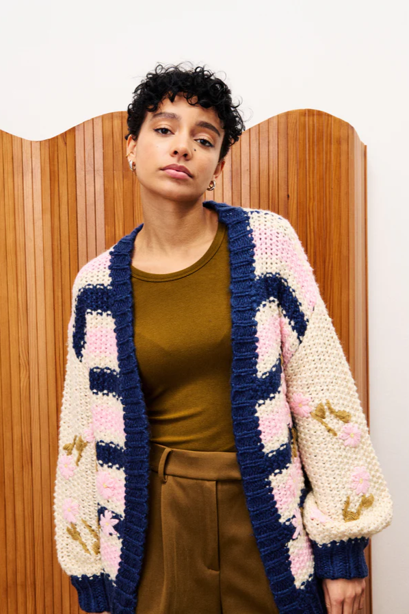 Person wearing a colorful crocheted cardigan against a wooden panel background
