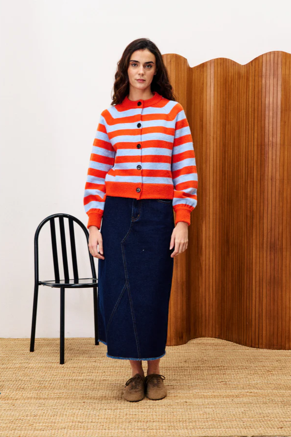 Woman wearing a red and orange striped sweater with a wooden wall and black chair in the background