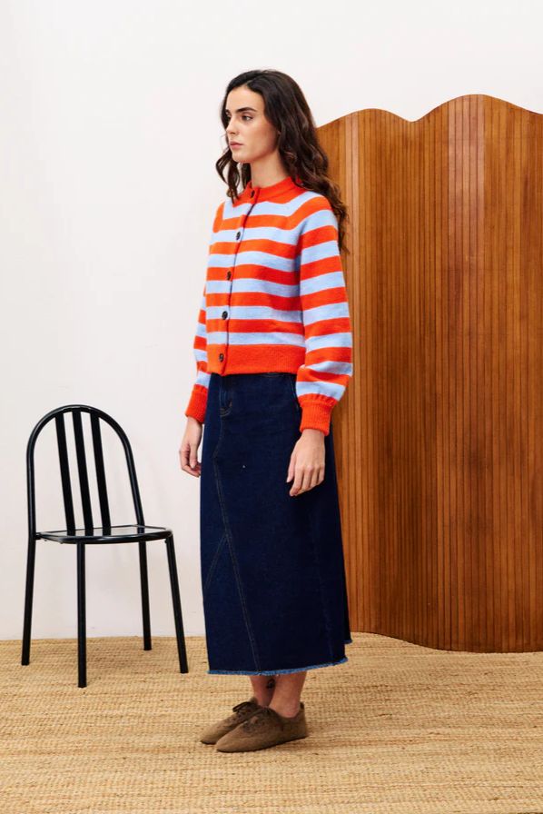 Woman wearing a red and blue striped sweater with a black chair and wooden panel in the background.