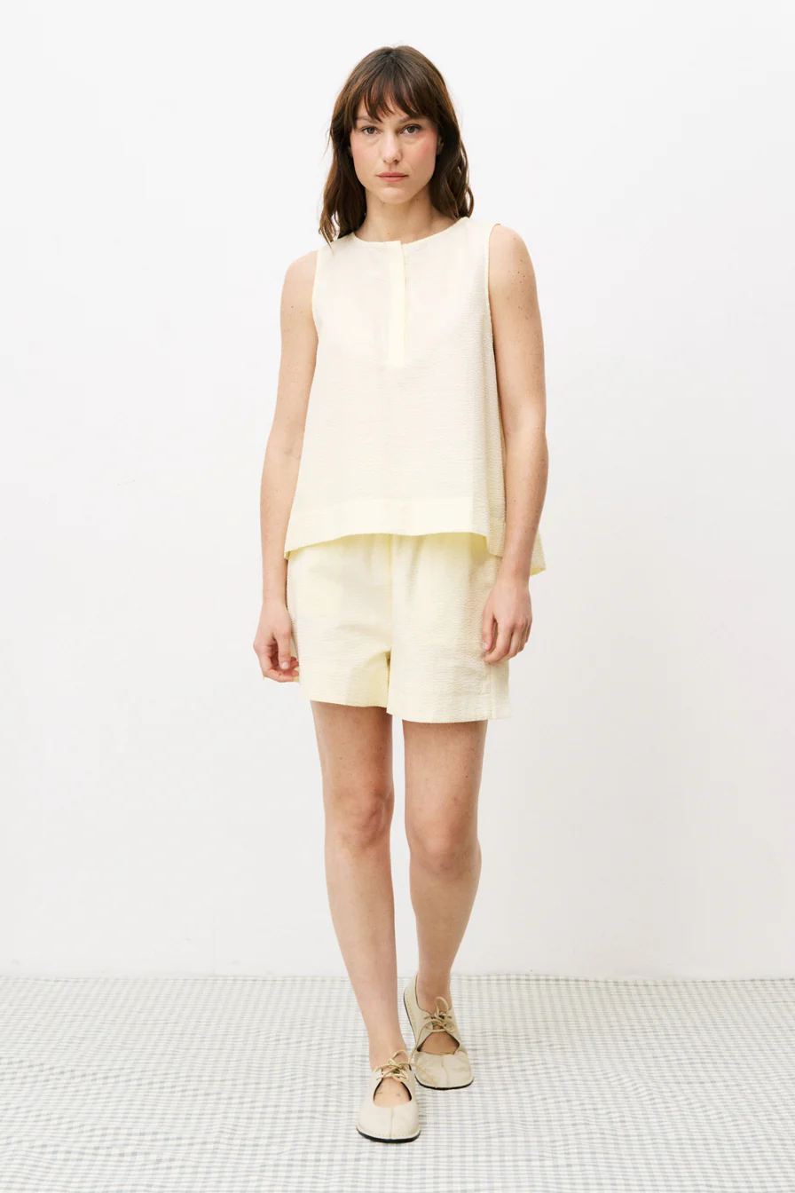 Woman wearing a light yellow sleeveless top and shorts on a white background