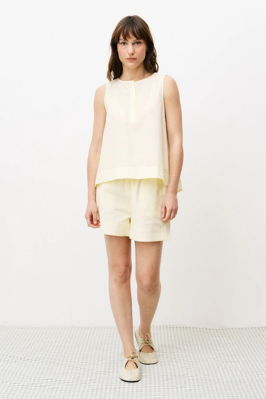 Woman wearing a light yellow sleeveless top and shorts on a white background