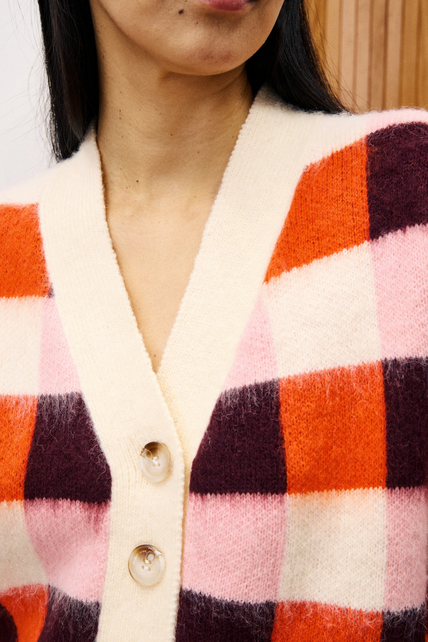 Close-up of a person wearing a colorful checkered cardigan with a neutral background