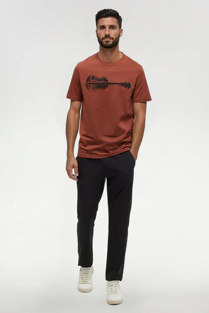 Man wearing a brown t-shirt with a graphic design and black pants on a white background