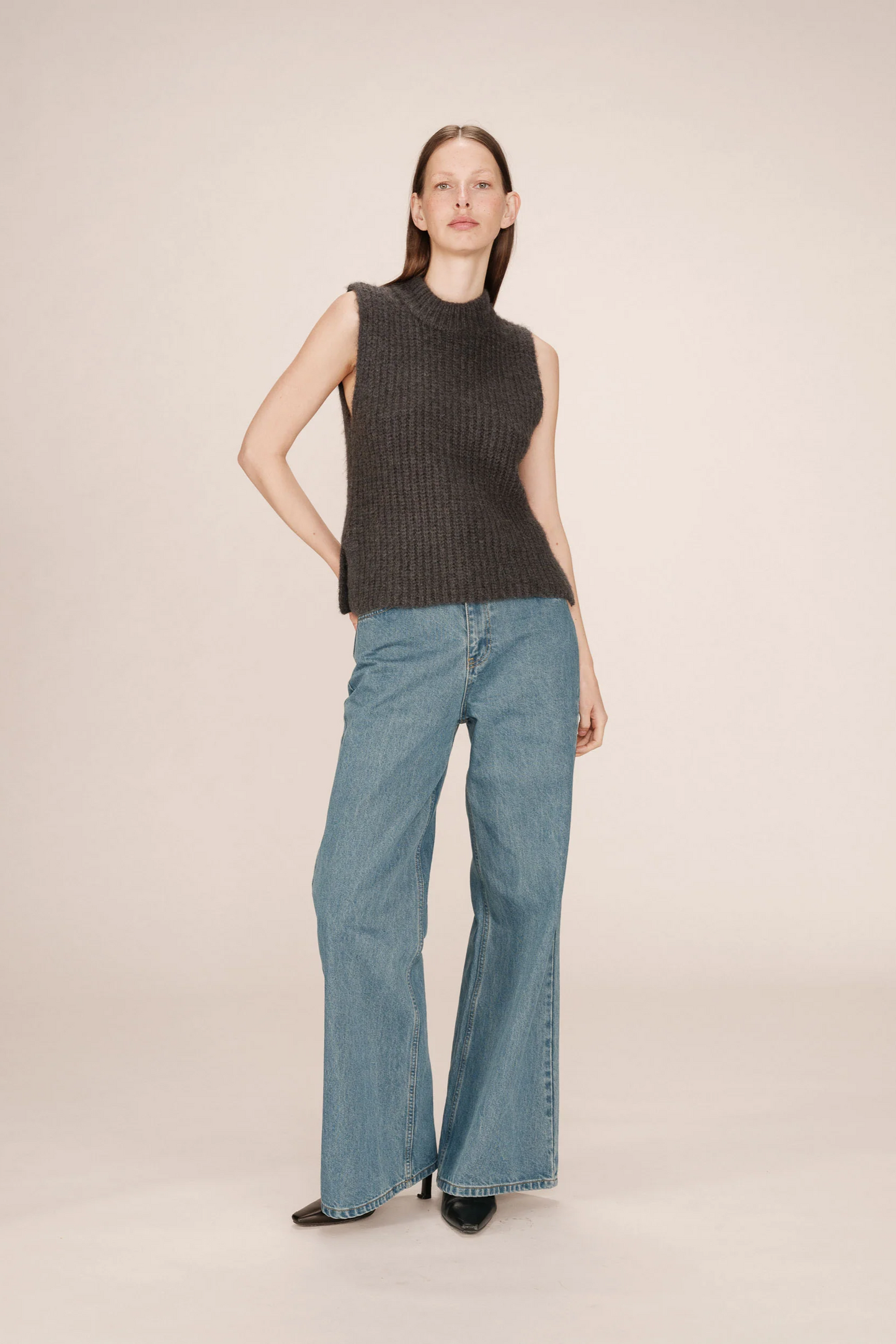 Woman wearing a sleeveless dark top and light blue jeans on a beige background