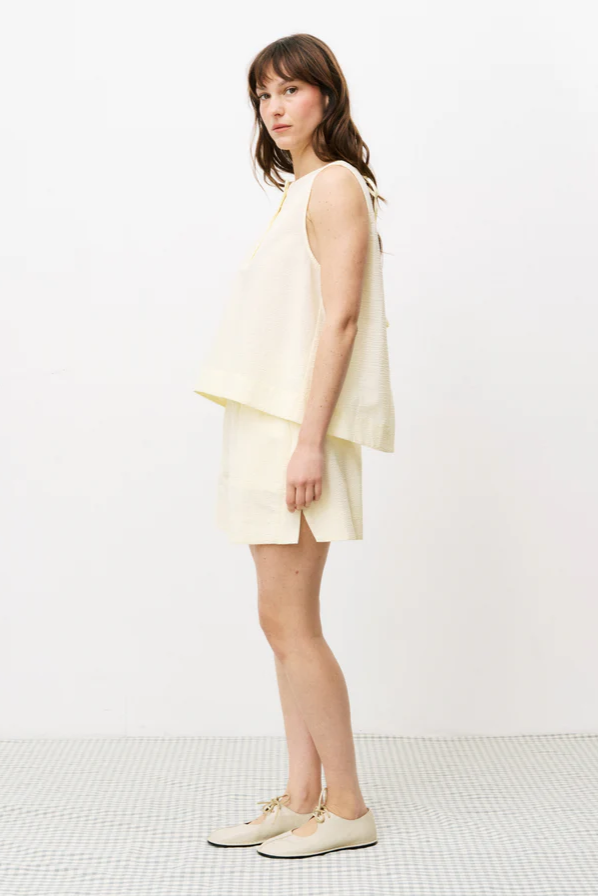 Woman wearing a light yellow sleeveless top and shorts on a white background