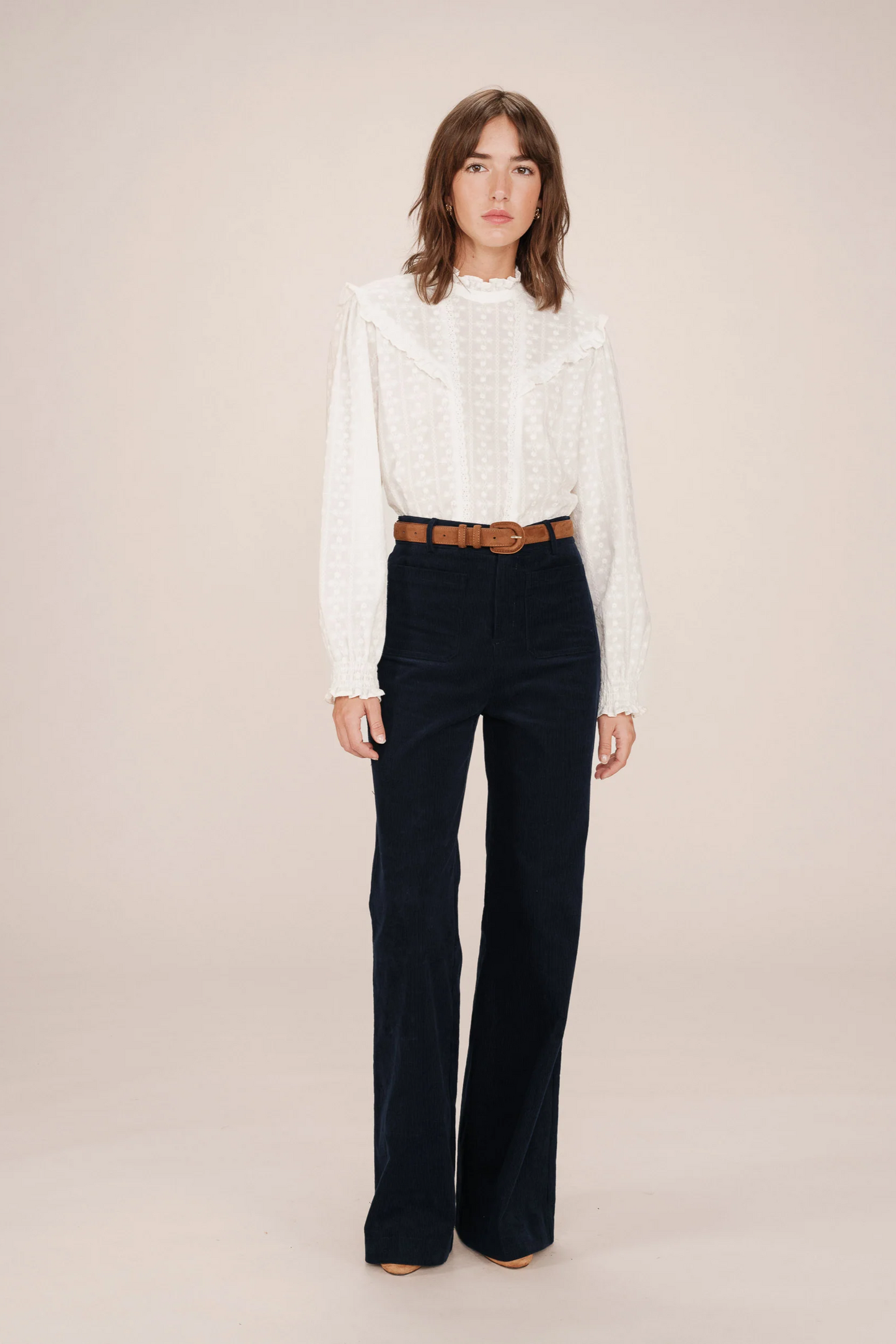 Woman wearing a white blouse and dark blue pants on a beige background