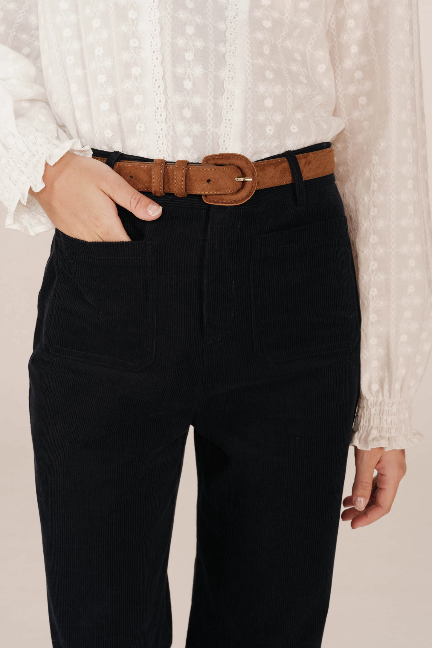 Person wearing black pants with a brown belt and white blouse on a beige background