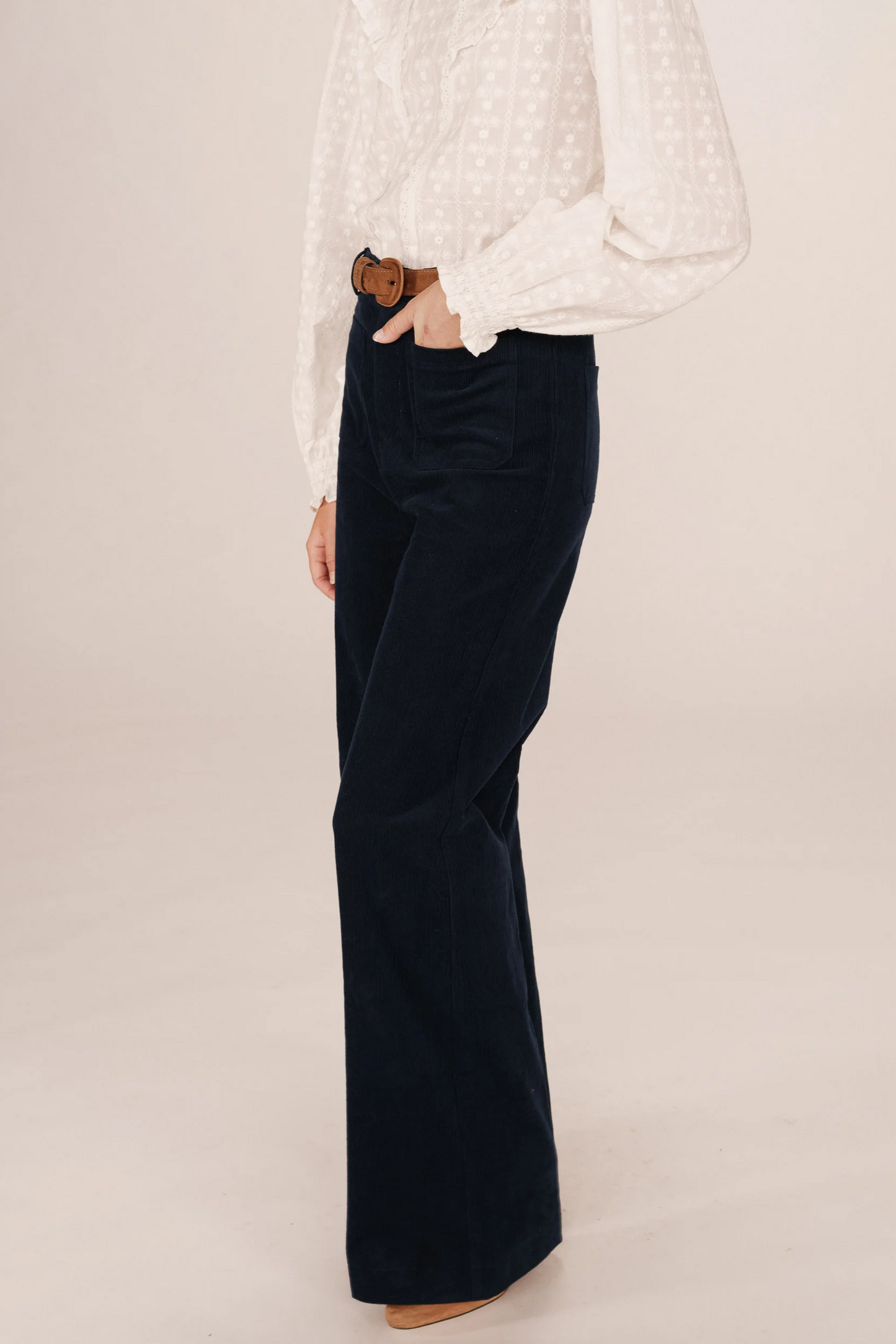 Navy velvet wide-leg pants worn with a white blouse on a plain background