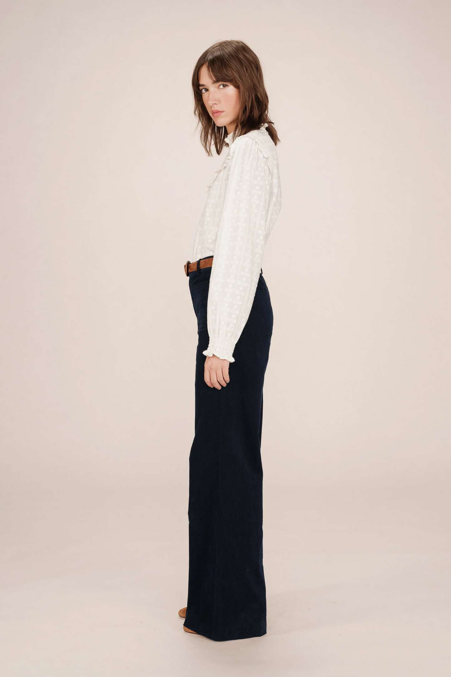 Woman wearing a white blouse and dark pants on a plain background
