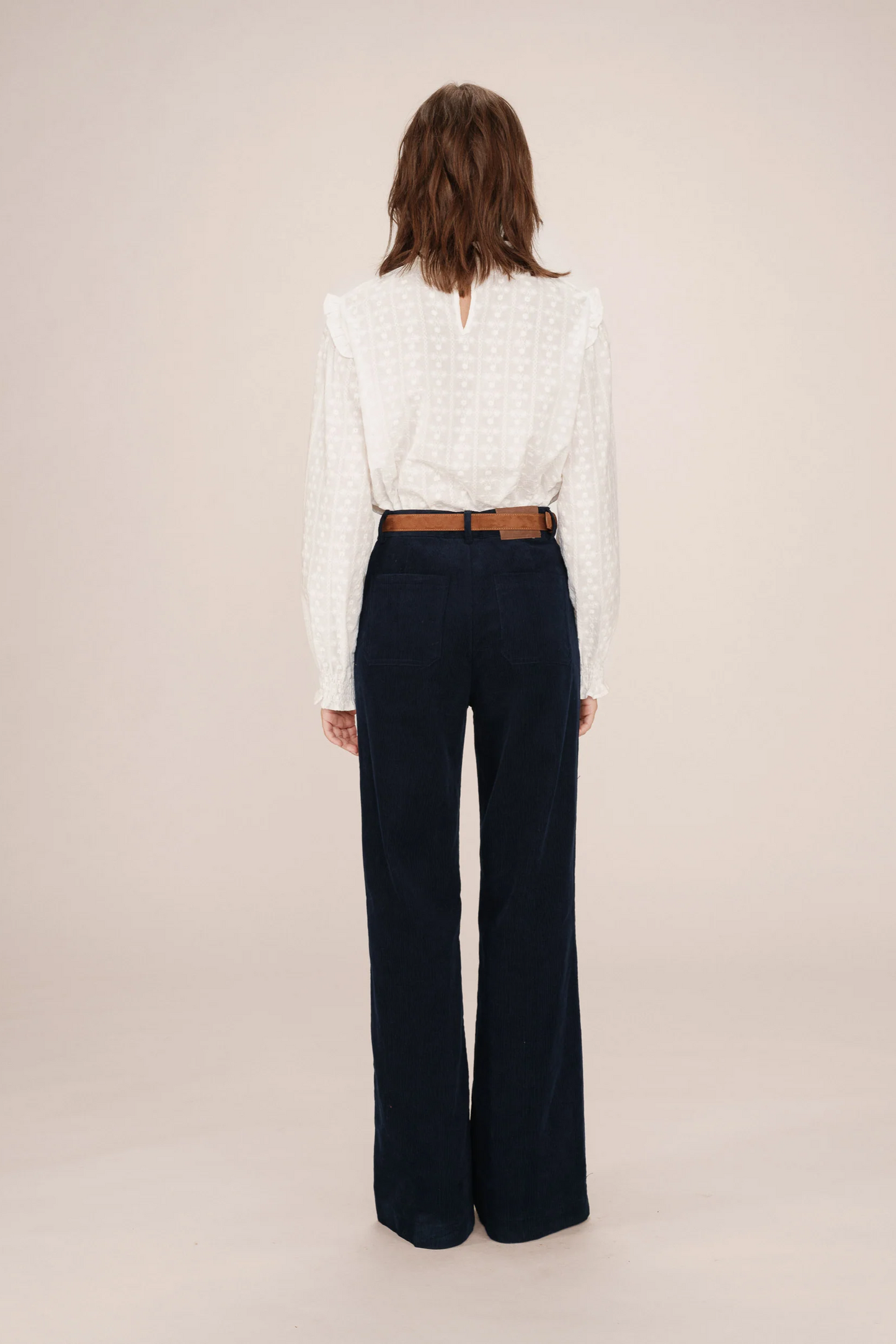 Person wearing a white blouse and dark blue pants on a beige background