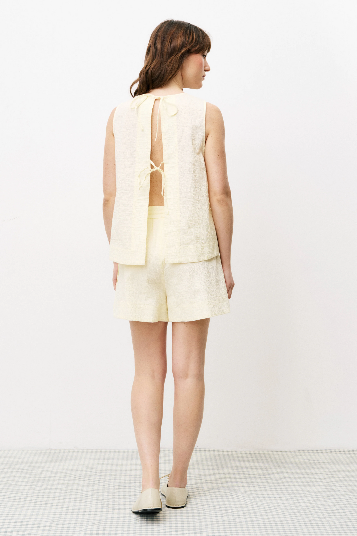 Woman wearing a light-colored sleeveless top and shorts set on a white background