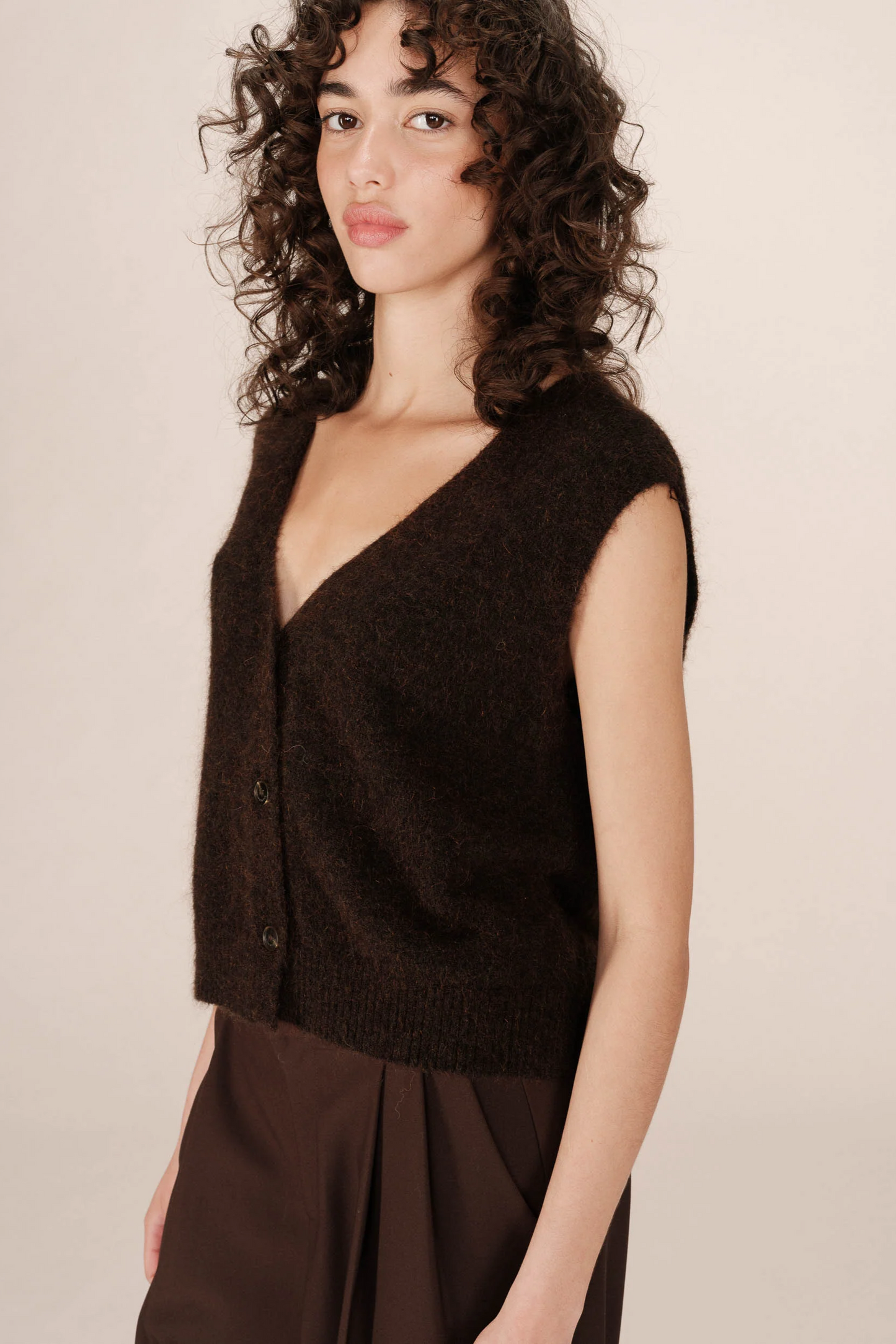 Woman wearing a brown sleeveless knitted top against a beige background