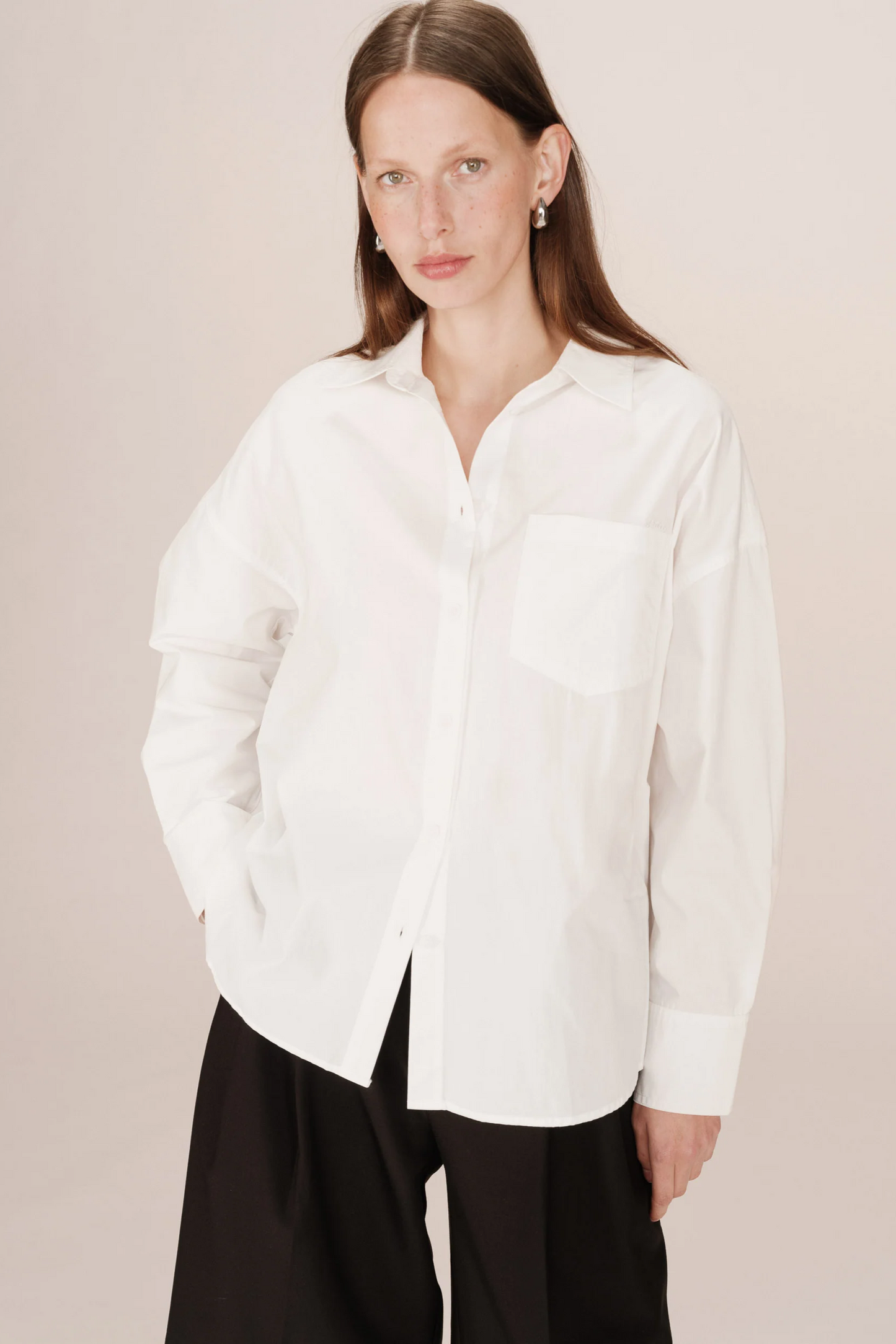Woman wearing a white shirt and black pants against a plain background
