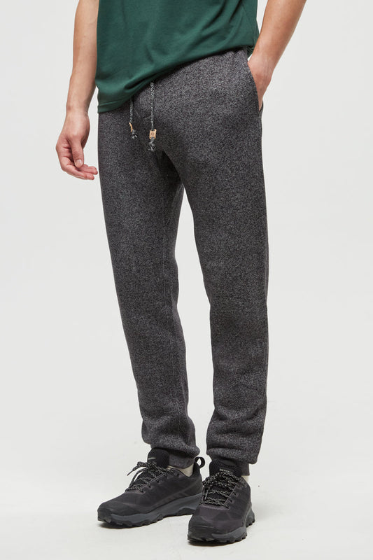 Person wearing dark gray jogger pants and black shoes on a white background