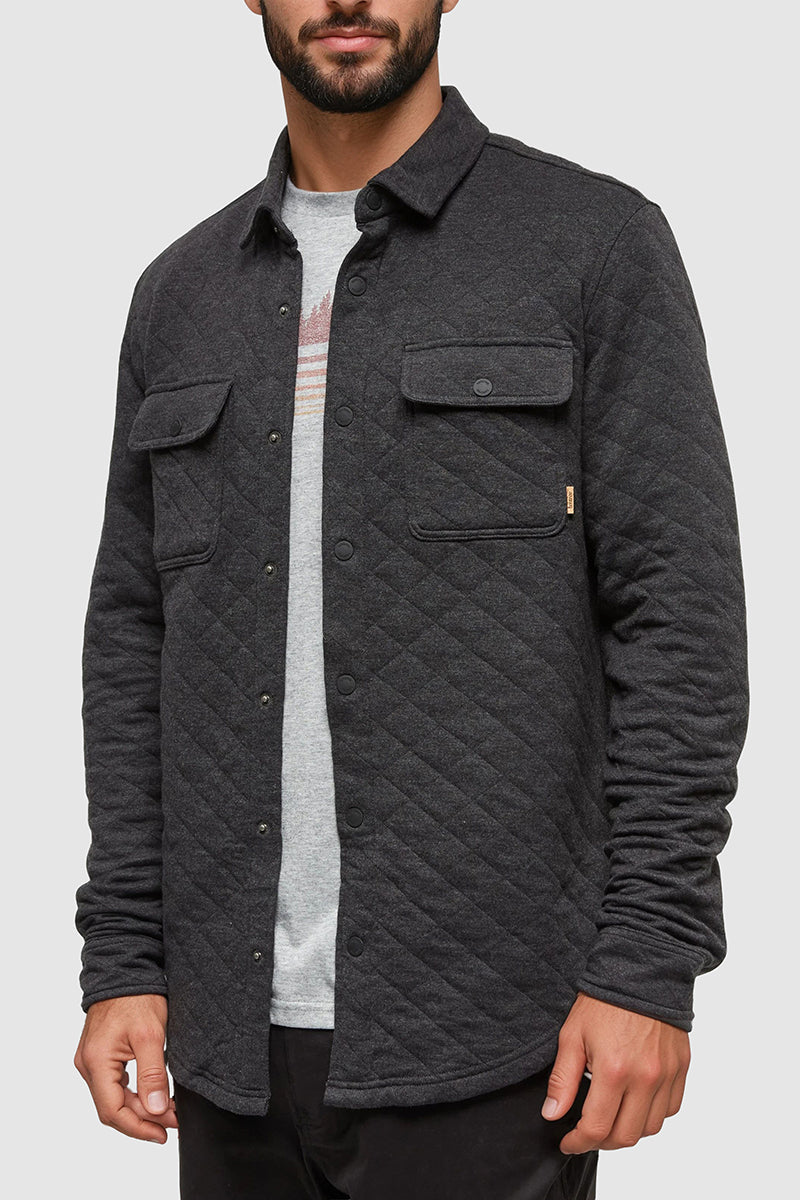 Man wearing a dark gray quilted jacket over a light gray shirt on a white background