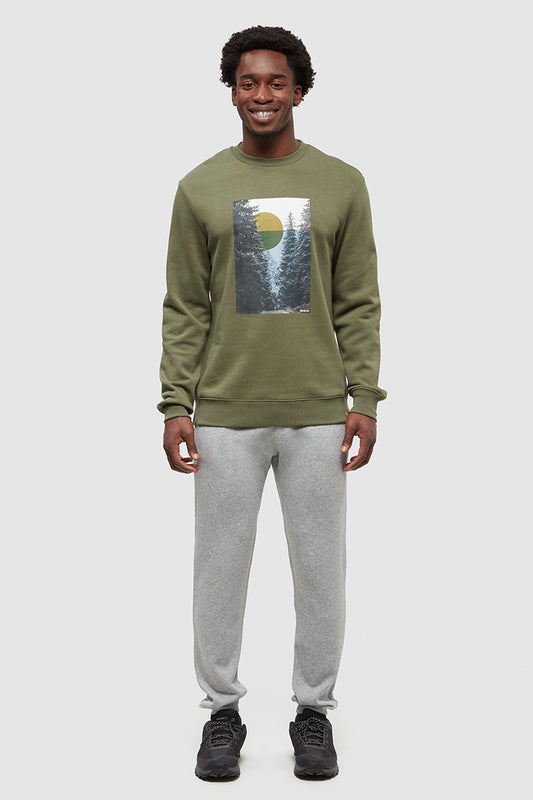 Person wearing a green sweatshirt with a forest graphic and gray pants on a white background
