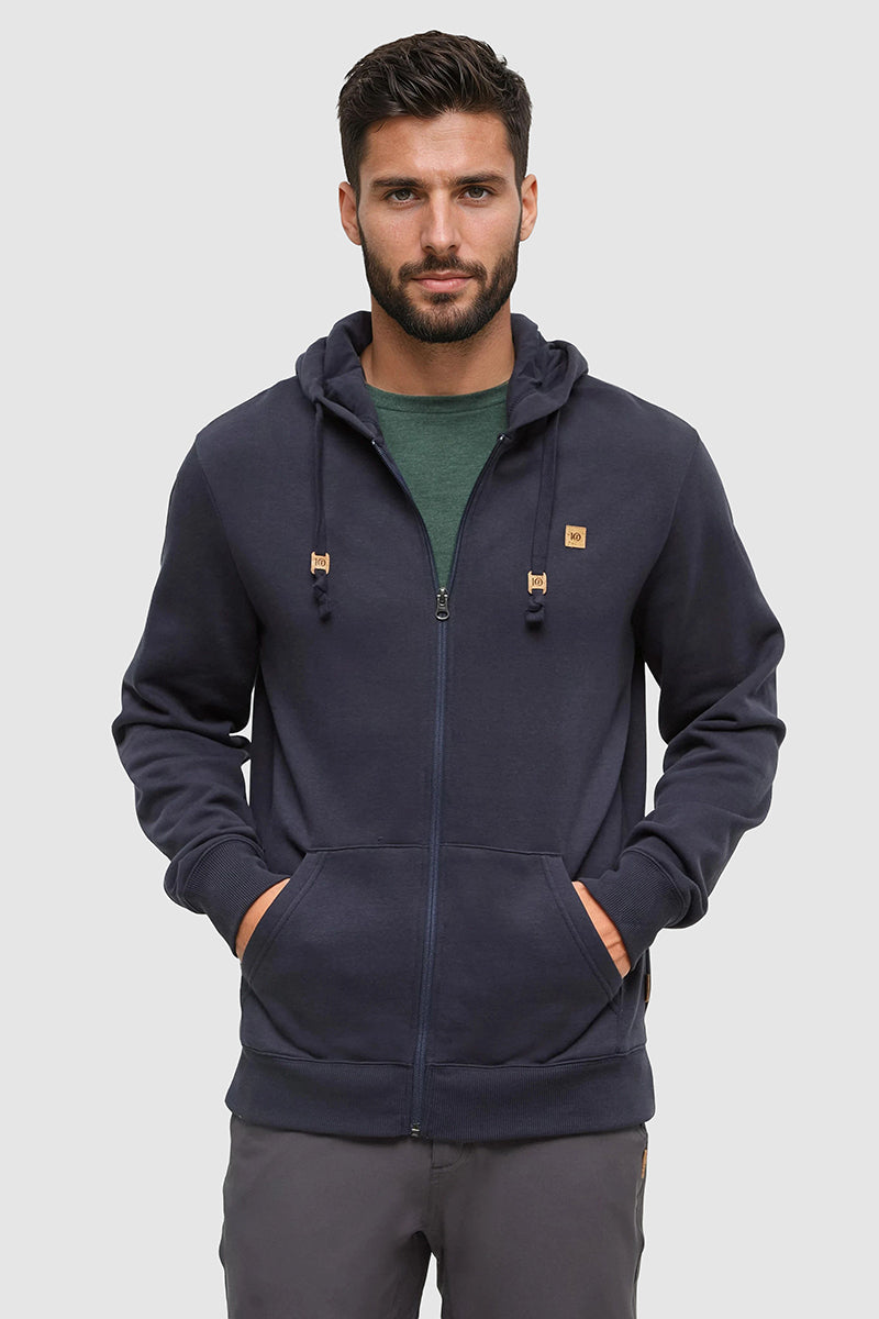 Man wearing a navy blue hoodie with brand logos on a light gray background