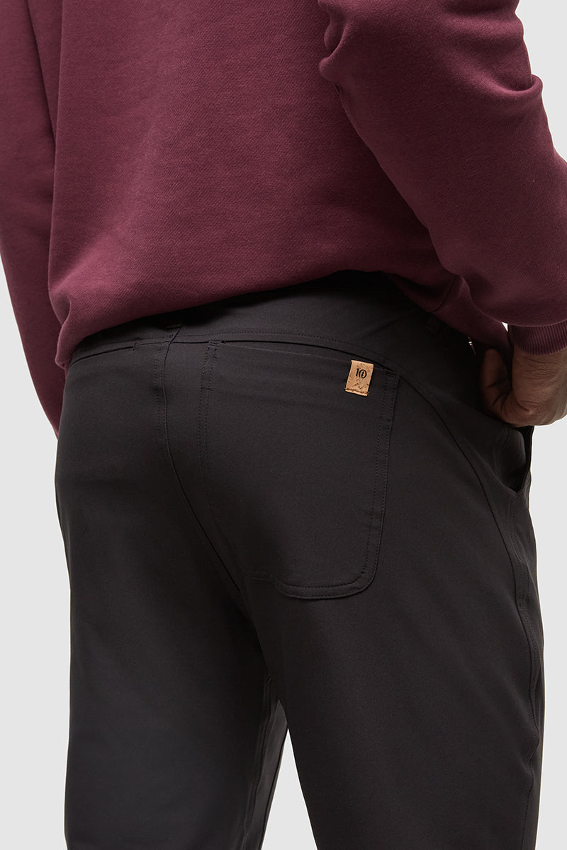 Person wearing black pants with a visible brand logo on a light gray background