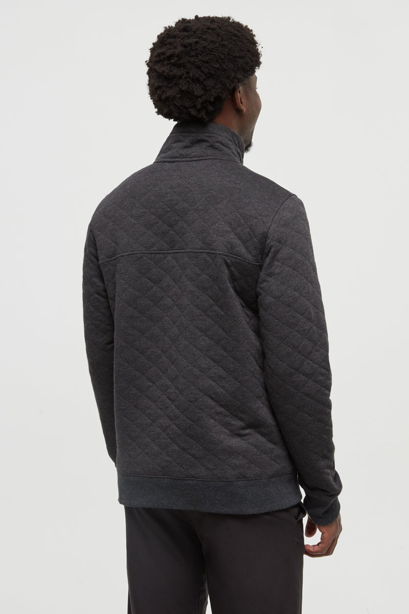 Person wearing a dark gray quilted jacket on a light gray background