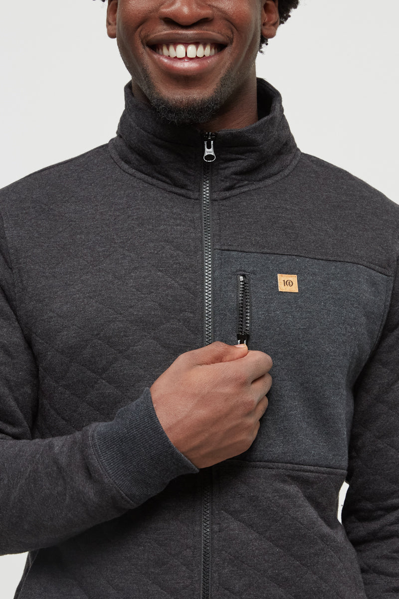 Man wearing a dark gray quilted jacket with a brand logo on a light gray background