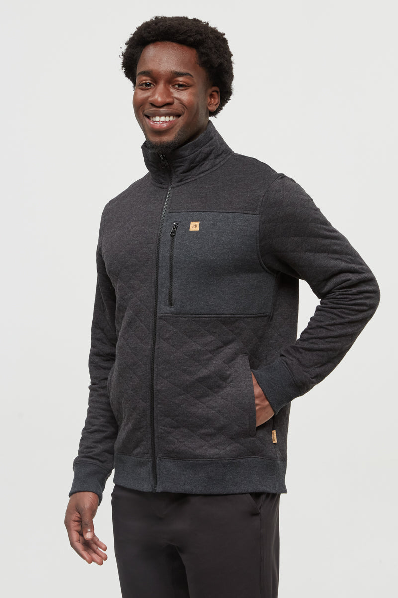 Man wearing a dark gray jacket with a brand logo on a light gray background