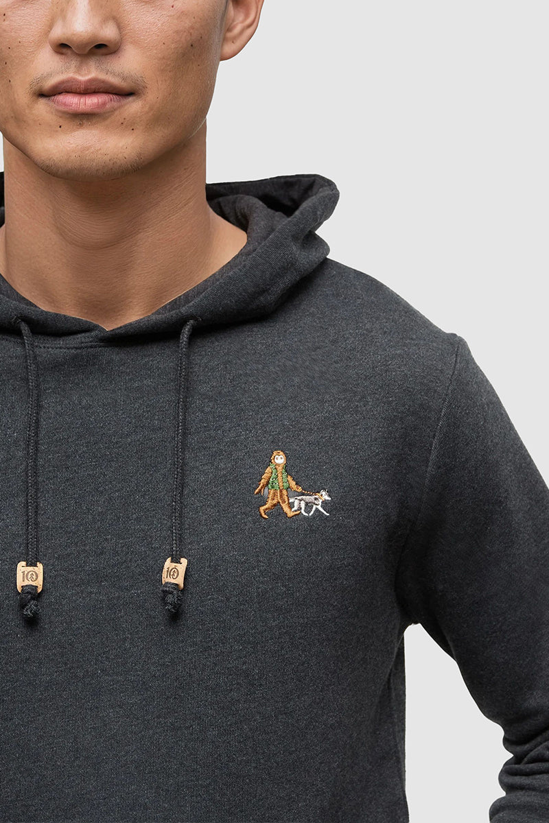 Person wearing a dark gray hoodie with a small embroidered design on a plain background