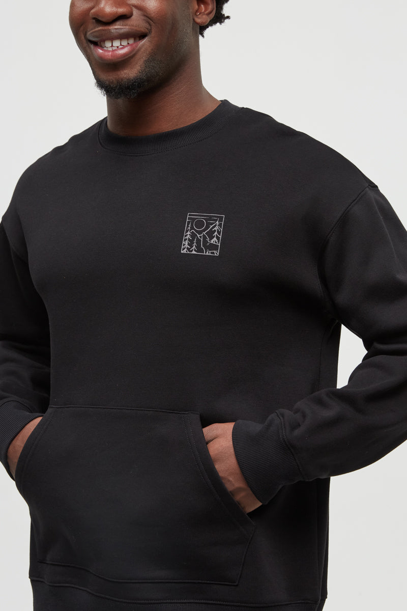 Person wearing a black sweatshirt with a small logo on a plain background