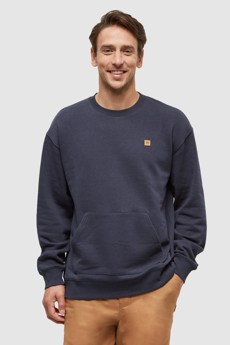 Man wearing a navy blue sweatshirt with a small logo on a plain background